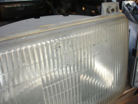 1992 Ford F-350 - Close-up of a vehicle's clear plastic headlight lens, showing internal fluting and condensation.