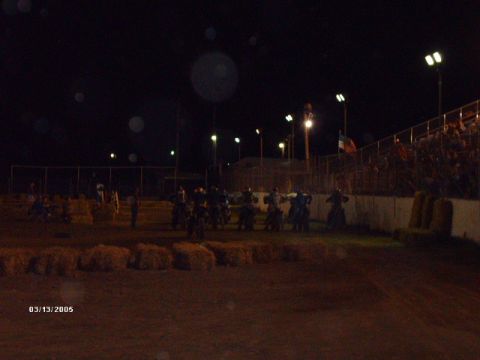 1995 Ford Probe - A group of motorcycles are gathered on a dirt track under stadium lights at night, with spectators in the stands.