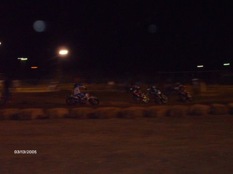 1995 Ford Probe - Several motorcycles are racing on a dirt track at night under artificial lighting.