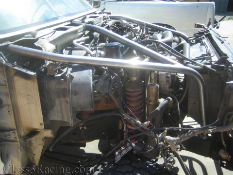 1990 Ford Bronco - Close view into a project truck's engine bay showing a red coilover spring, tubular chassis bracing, an alternator and a tangle of wiring a…