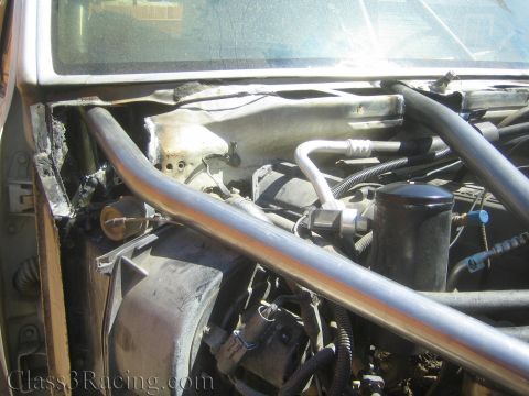 1990 Ford Bronco - Detail of a bare-metal tube brace crossing the cowl and firewall area of a stripped vehicle, beside a black blower housing and bundled wiri…