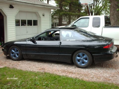 1995 Ford Probe - A black coupe with custom blue wheels is parked next to a garage, with a white pickup truck behind it.