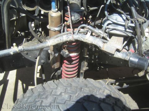 1990 Ford Bronco - Front suspension of a project truck showing a red coilover spring, steering linkage and braided hoses above an off-road tire.