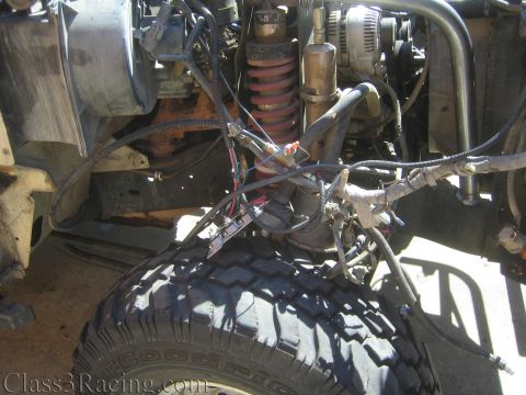 1990 Ford Bronco - Underhood view of a project truck's lower front end showing a red coilover, alternator, wiring harness and a mud-terrain tire below.