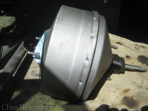1990 Ford Bronco - silver power brake booster bolted to a firewall, its pushrod and mounting studs visible, set above a stained tan drop cloth.