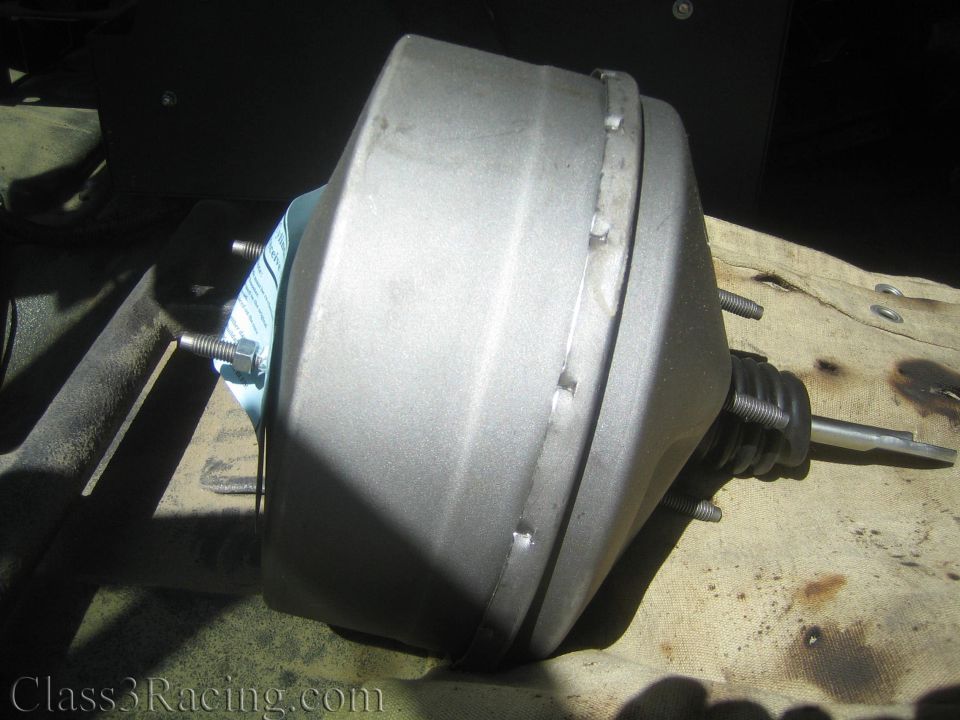 Silver power brake booster mounted to a firewall over a tan drop cloth