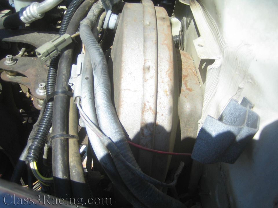 Engine-bay detail of a large round metal canister with wiring and foam padding