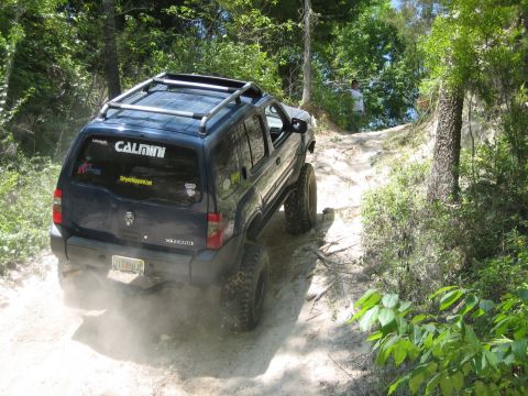1989 Ford Bronco - SUV navigates a dusty off-road trail surrounded by trees.