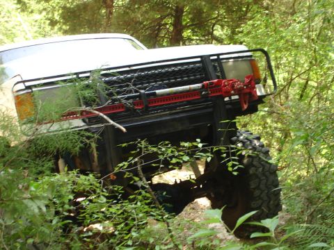 1989 Ford Bronco - This 1989 Ford Bronco is equipped with a red Hi-Lift jack on its front bumper, tackling challenging off-road conditions.