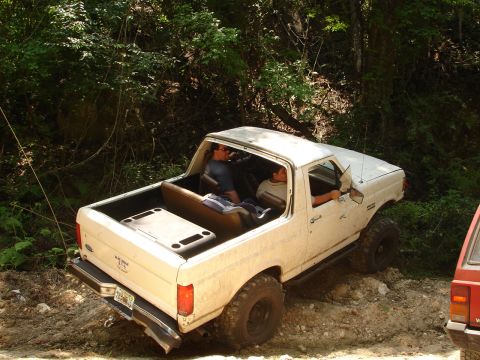 1989 Ford Bronco - White 1989 Ford Bronco navigates a wooded trail with passengers.