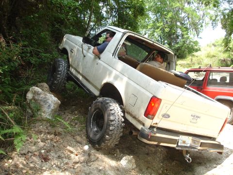 1989 Ford Bronco - This white Ford Bronco is navigating a challenging off-road trail, with a red Jeep following closely behind.