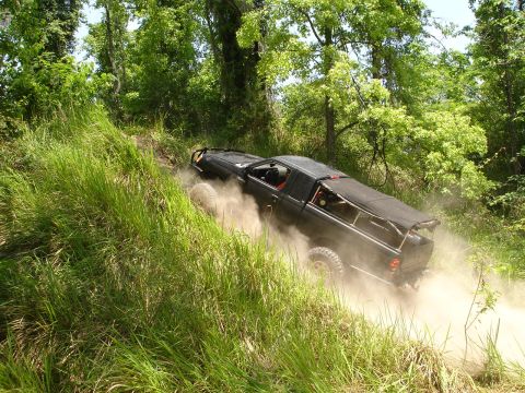 1989 Ford Bronco - Off-road vehicle navigates a steep, dusty trail surrounded by dense vegetation.