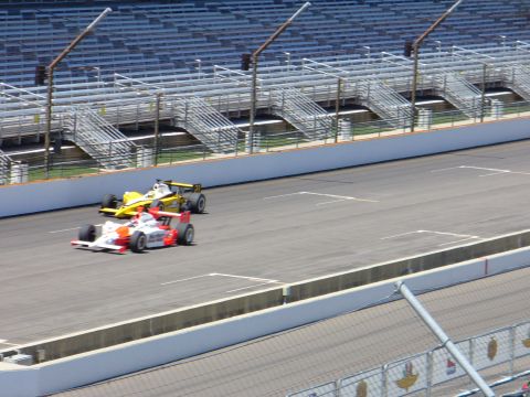 1991 Ford Probe - Two race cars compete on a sunny day at the speedway, with empty bleachers overlooking the track.