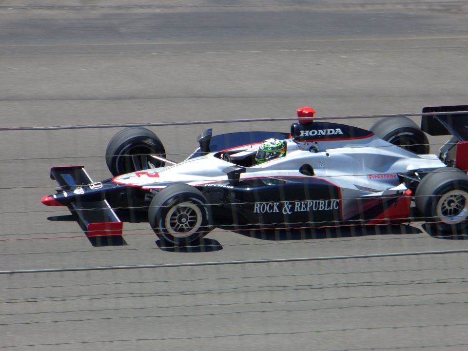 Silver and black IndyCar with red accents, number 2, driven by a person in a green helmet