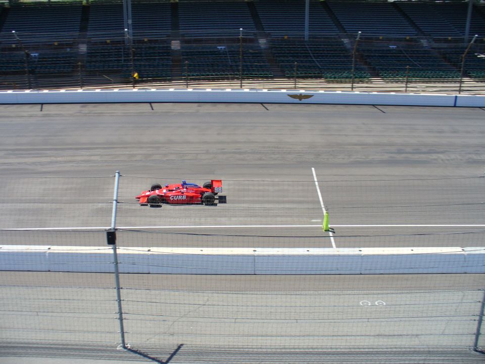Red open-wheel race car on a track, with grandstands in the background