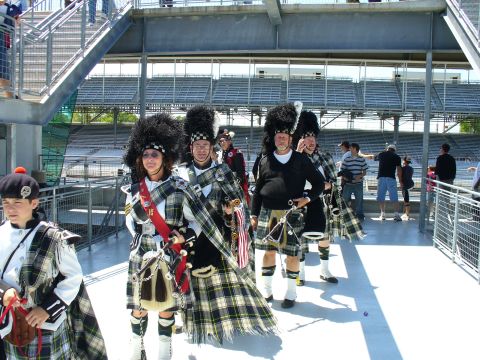 1991 Ford Probe - A bagpipe band marches in kilts and feathered hats, with stadium seating in the background.