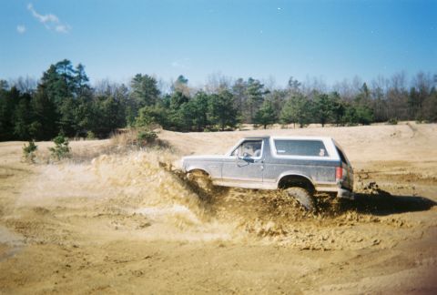 1989 Ford Bronco - A Ford Bronco navigates a muddy terrain, kicking up a large splash.