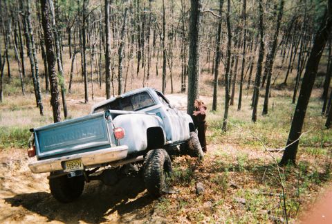 1989 Ford Bronco - A light blue pickup truck is parked off-road in a wooded area with a person standing beside it.