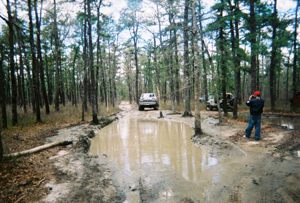 White 1989 Ford Bronco driving through muddy forest road