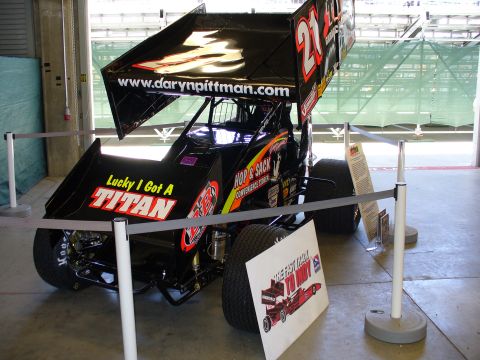 1991 Ford Probe - A black racing sprint car with sponsor decals is displayed behind a barrier.
