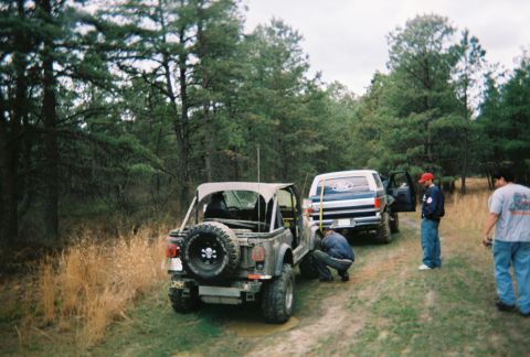 1989 Ford Bronco - A group of people and vehicles are gathered on a dirt road in a wooded area.