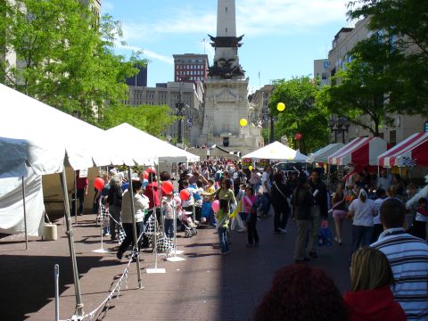 1991 Ford Probe - A busy street fair is taking place in front of a large monument, with many people browsing stalls under tents.