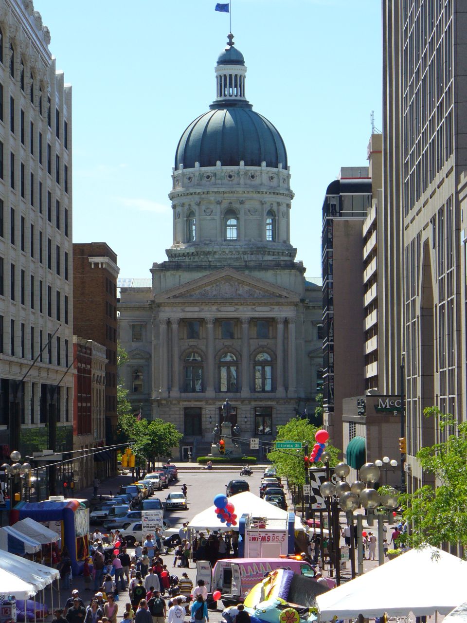 Street scene with a large domed building, crowds of people, tents, and cars