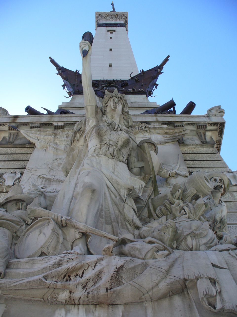 Monumental sculpture depicting figures, cannons, and a ship's prow against a blue sky