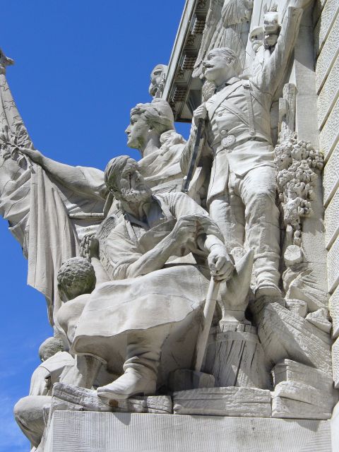 1991 Ford Probe - A detailed stone sculpture depicts several figures, some holding a flag and others tools, against a bright blue sky.