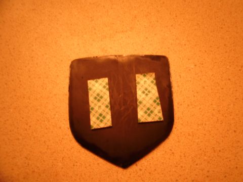 1996 Ford Probe - A dark emblem with adhesive strips is shown against an orange textured background.