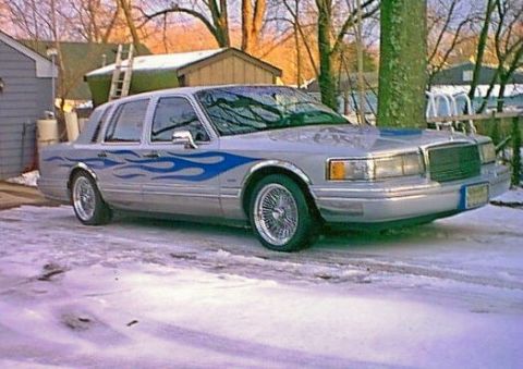 1998 Lincoln Town Car - A silver sedan with blue flame decals sits in a snowy driveway, wire wheels and chrome accents.