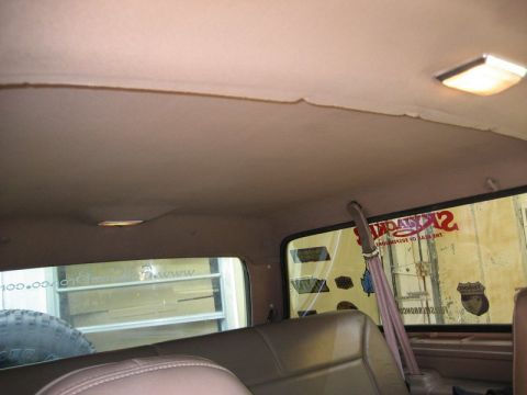 1995 Ford Bronco - The interior of a vehicle shows the headliner, seats, and a rear window with various stickers.
