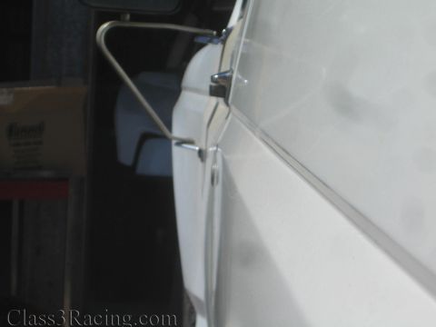 1990 Ford Bronco - Extreme close-up of a chrome tubular bracket running along the edge of a white painted body panel in dim shop light.