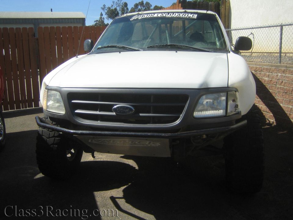 Front of a white lifted Ford pickup with black bumper and Ford-grille emblem