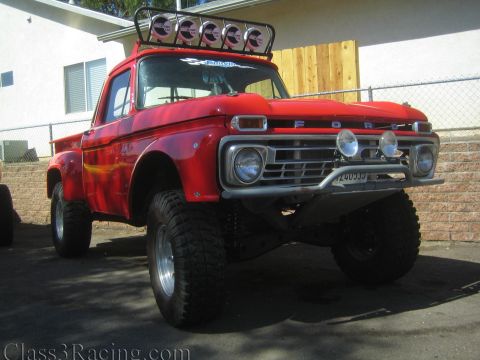1990 Ford Bronco - Front three-quarter view of a red lifted Ford pickup with FORD lettering on the hood, chrome bumper, light bar and big off-road tires.