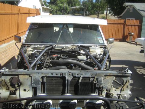 1990 Ford Bronco - front of a stripped race truck with hood removed, exposing the engine, tubular cage, and radiator support.
