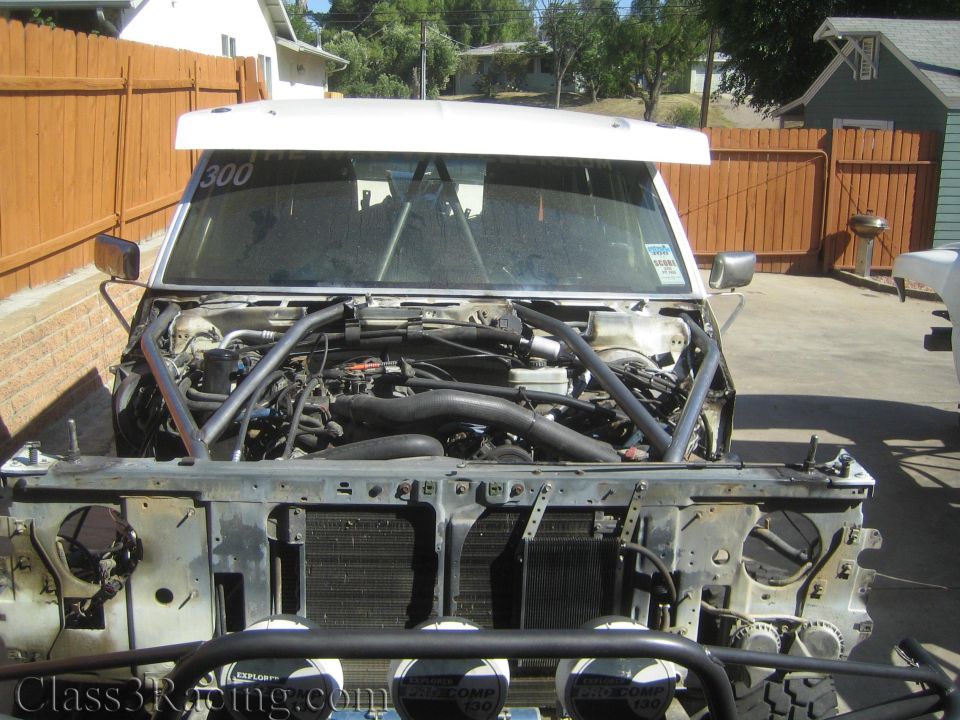 Open engine bay of a stripped truck showing engine, roll cage, and radiator