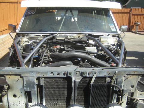 1990 Ford Bronco - Close-up of a race truck engine bay with thick black radiator hoses, roll cage tubing, and an exposed radiator.