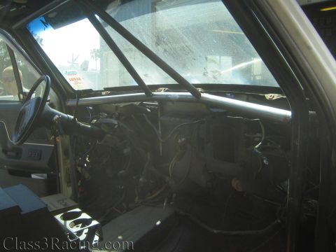 1990 Ford Bronco - stripped interior of a truck cab showing the steering wheel, roll cage bar, and exposed dashboard wiring.