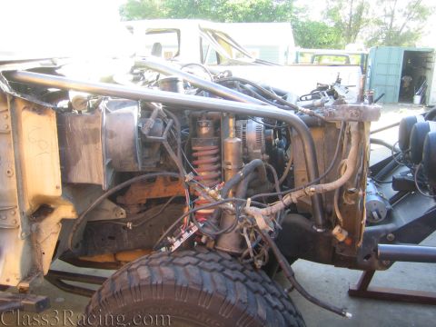1990 Ford Bronco - Side view of a stripped truck front end showing the engine, coilover shock, and a mud-terrain front tire.