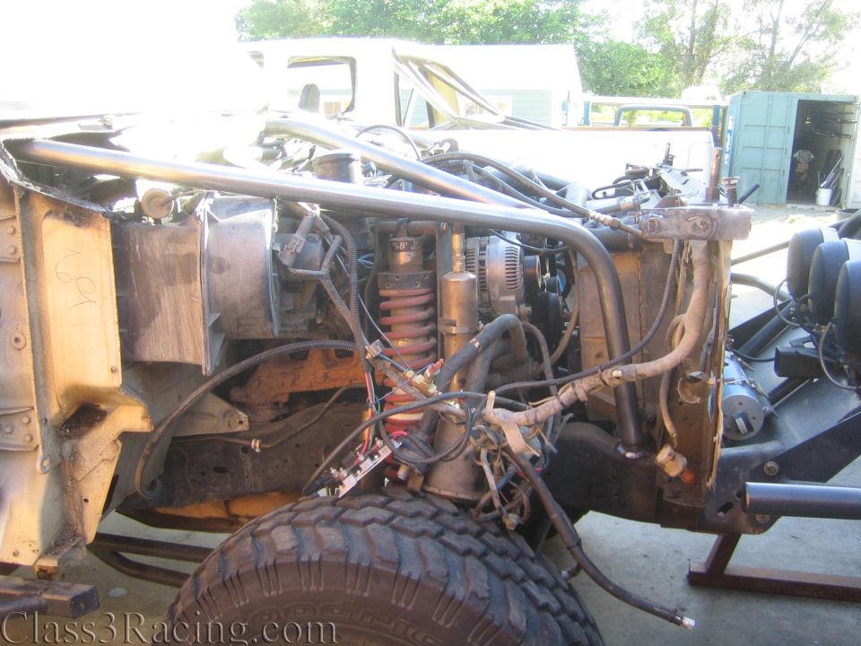 Side view of a stripped truck front end with engine, coilover and front tire
