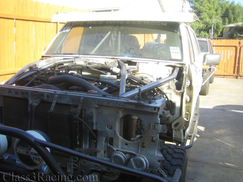Front of a stripped truck with hood removed showing engine and Pro Comp lights