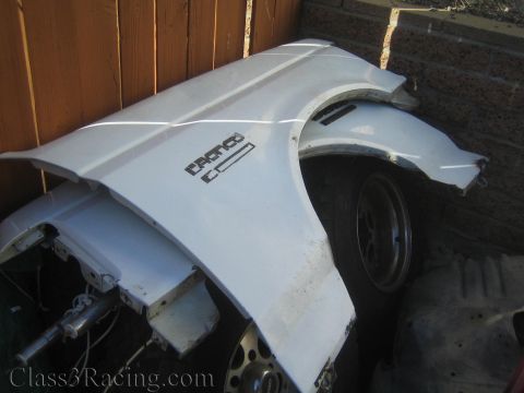 1990 Ford Bronco - Two white Ford fenders with embossed badging lean against a fence outdoors, with wheels and parts behind them.