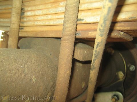 1990 Ford Bronco - Heavily rusted leaf spring, threaded U-bolts and an exhaust pipe are shown in a tight undercarriage view.
