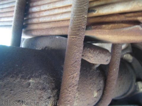 1990 Ford Bronco - Close-up of a corroded leaf spring and threaded U-bolt resting over a grimy suspension component.