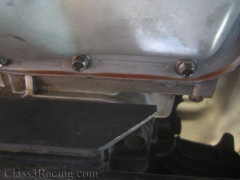 1990 Ford Bronco - underside of a metal pan with bolt heads, drain plugs and a sealant bead, mounted on a vehicle.