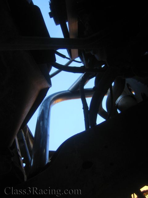 1990 Ford Bronco - Looking up through a fabricated tube chassis frame, with wiring and steel tubes silhouetted against blue sky.