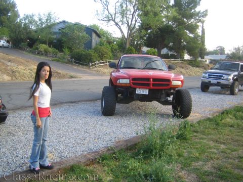 1990 Ford Bronco - woman stands beside a red lifted Dodge Dakota truck with large off-road tires parked on a gravel driveway.