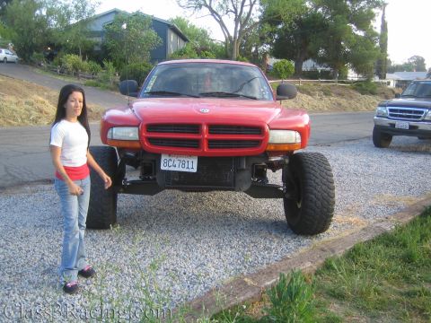 1990 Ford Bronco - woman poses beside the front bumper of a red lifted Dodge Dakota truck with large off-road tires outdoors.