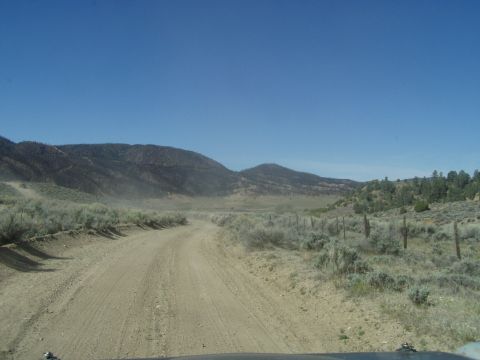 1967 Ford Bronco - Driving on a dusty dirt road in a remote, arid region with hills in the background.